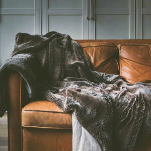 Dark gray fuzzy throw blanket on a leather couch.